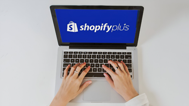 A user on their laptop with the screen showing the Shopify Plus logo
